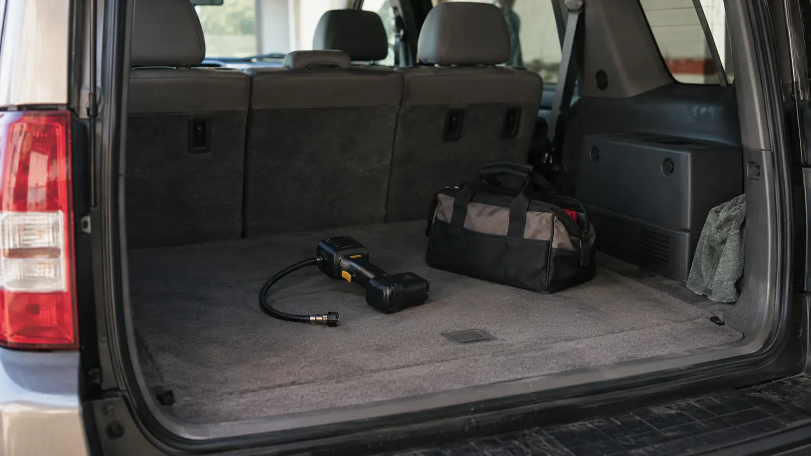 A cordless tire inflator on its side in an older SUV's cargo area next to a tool bag