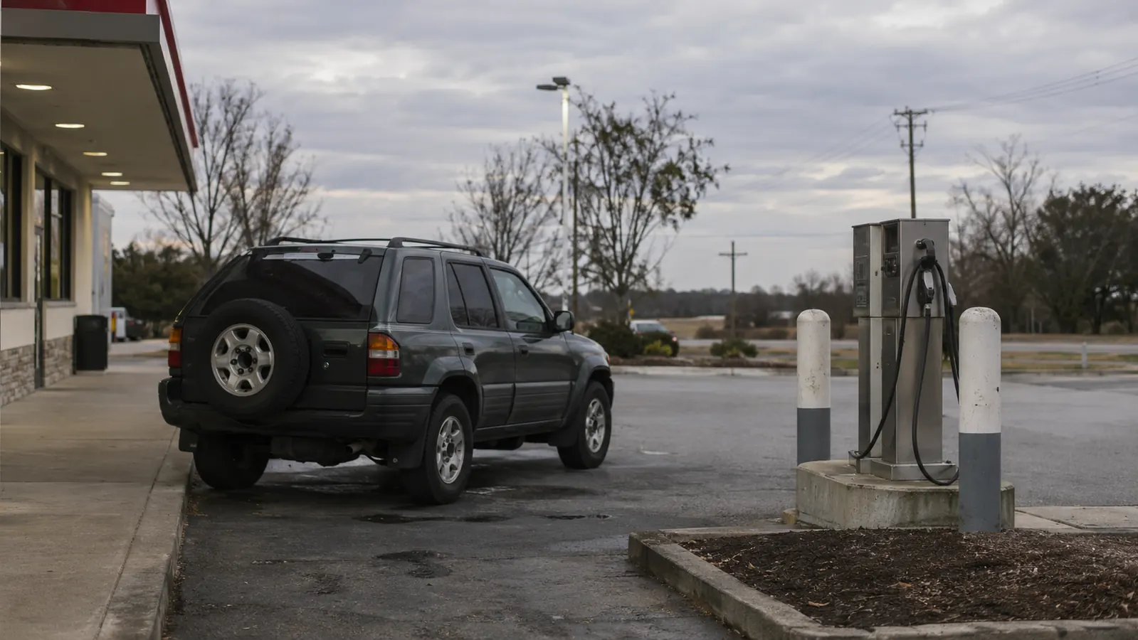 A self-serve air pump at a gas station with a long hose, and an older SUV parked beside it.