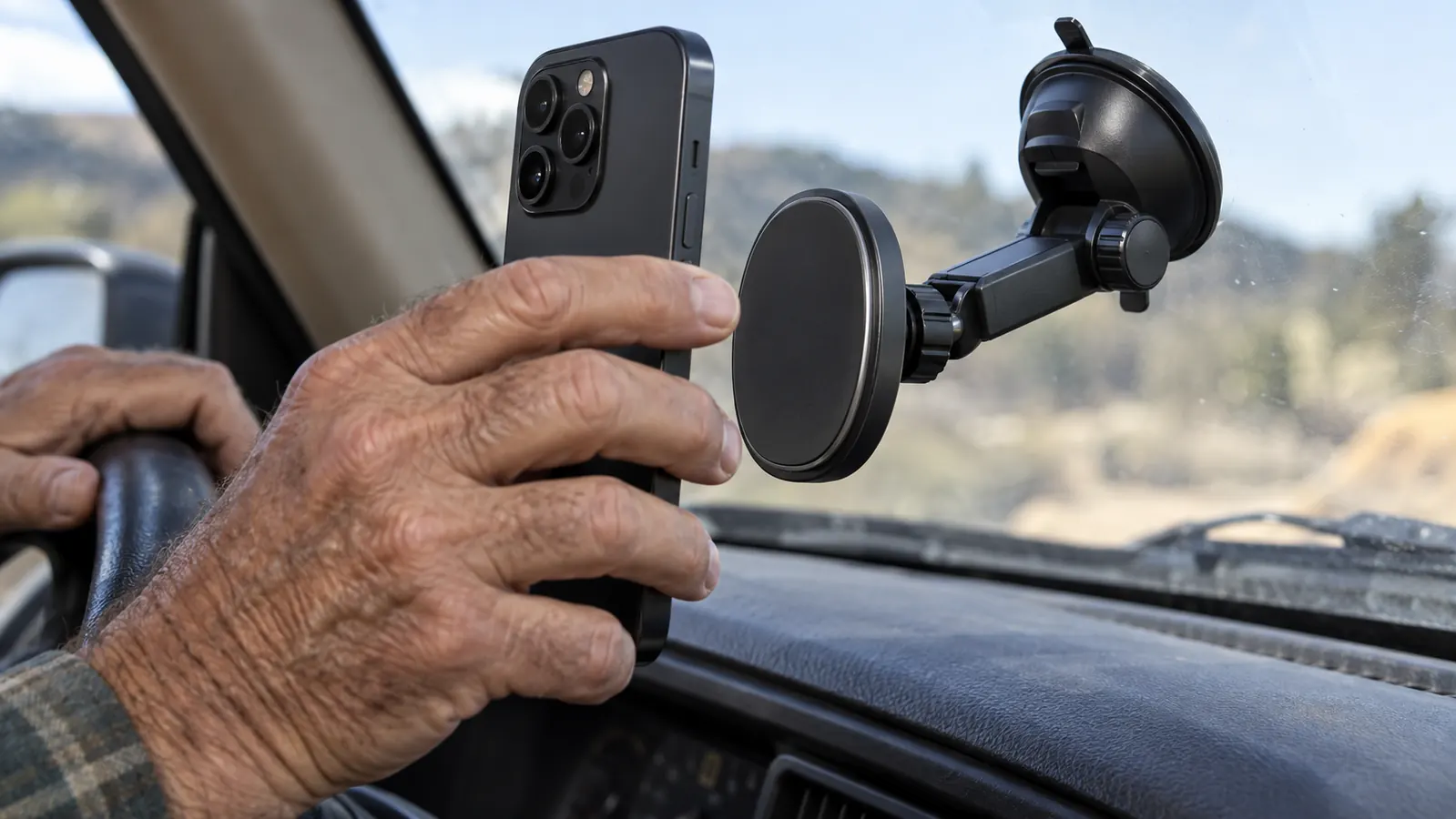 A hand placing a smartphone on a magnetic car mount that is attached to the windshield above the dashboard