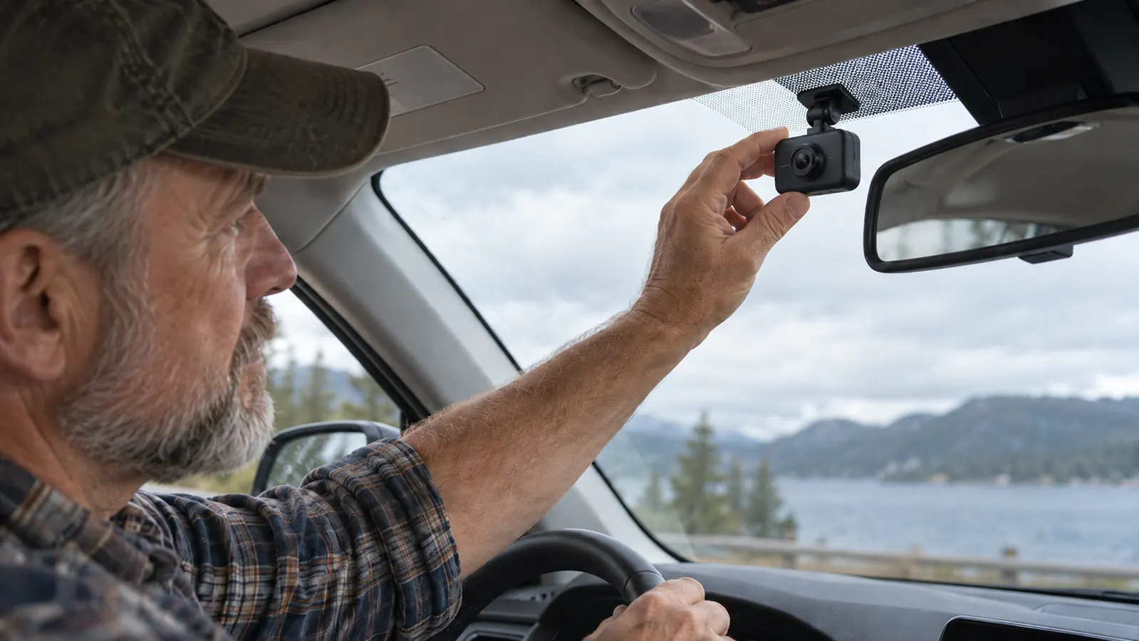 A driver's hand adjusts a dash cam mounted on the windshield of an older SUV.